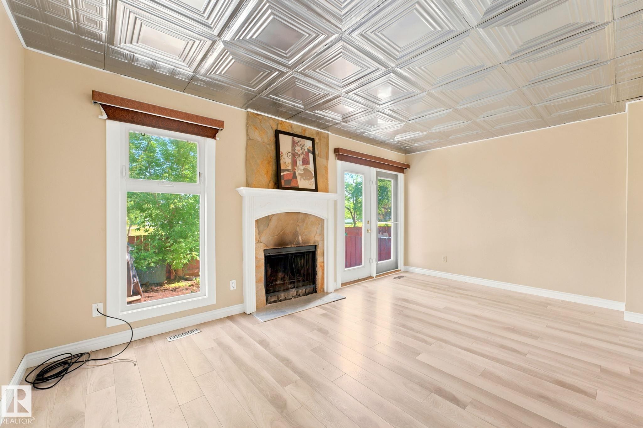 Spacious room featuring light wood-finish flooring, a decorative metal tile ceiling, and neutral wall tones - #41 4707 126 Av Nw, Edmonton, AB