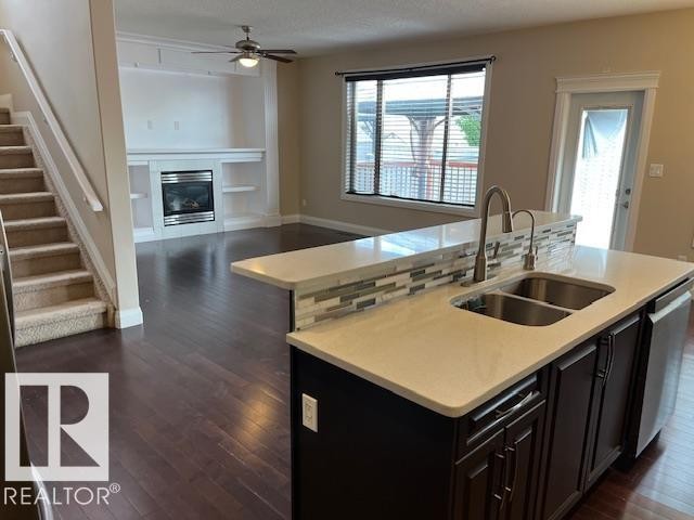Kitchen island featuring a double basin stainless steel sink with a gooseneck faucet, light-toned countertop, and mosaic tile backsplash - 805 Hodgins Road Nw, Edmonton, AB - Indoor Photo Showing Kitchen With Fireplace With Double Sink