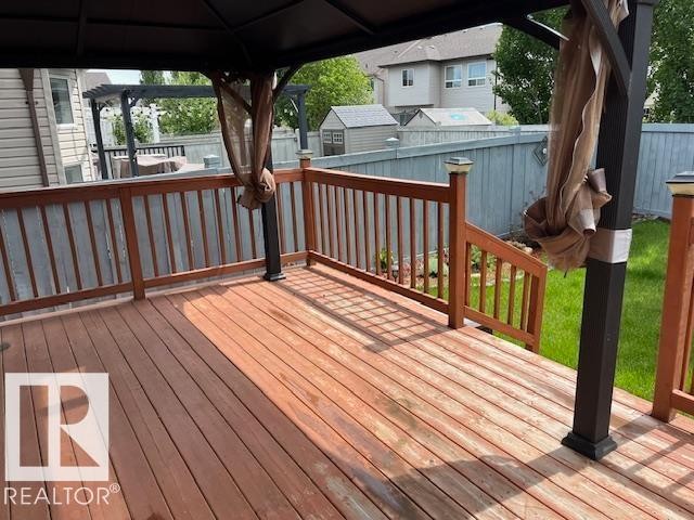 Spacious wood-finish deck featuring a dark metal gazebo structure with privacy screens, wood railings, and a manicured lawn area - 805 Hodgins Road Nw, Edmonton, AB - Outdoor With Deck Patio Veranda With Exterior