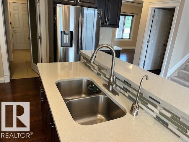 Kitchen island featuring a double basin stainless steel sink with a high-arch faucet, light-toned countertop, and a tiled backsplash - 805 Hodgins Road, Edmonton, AB