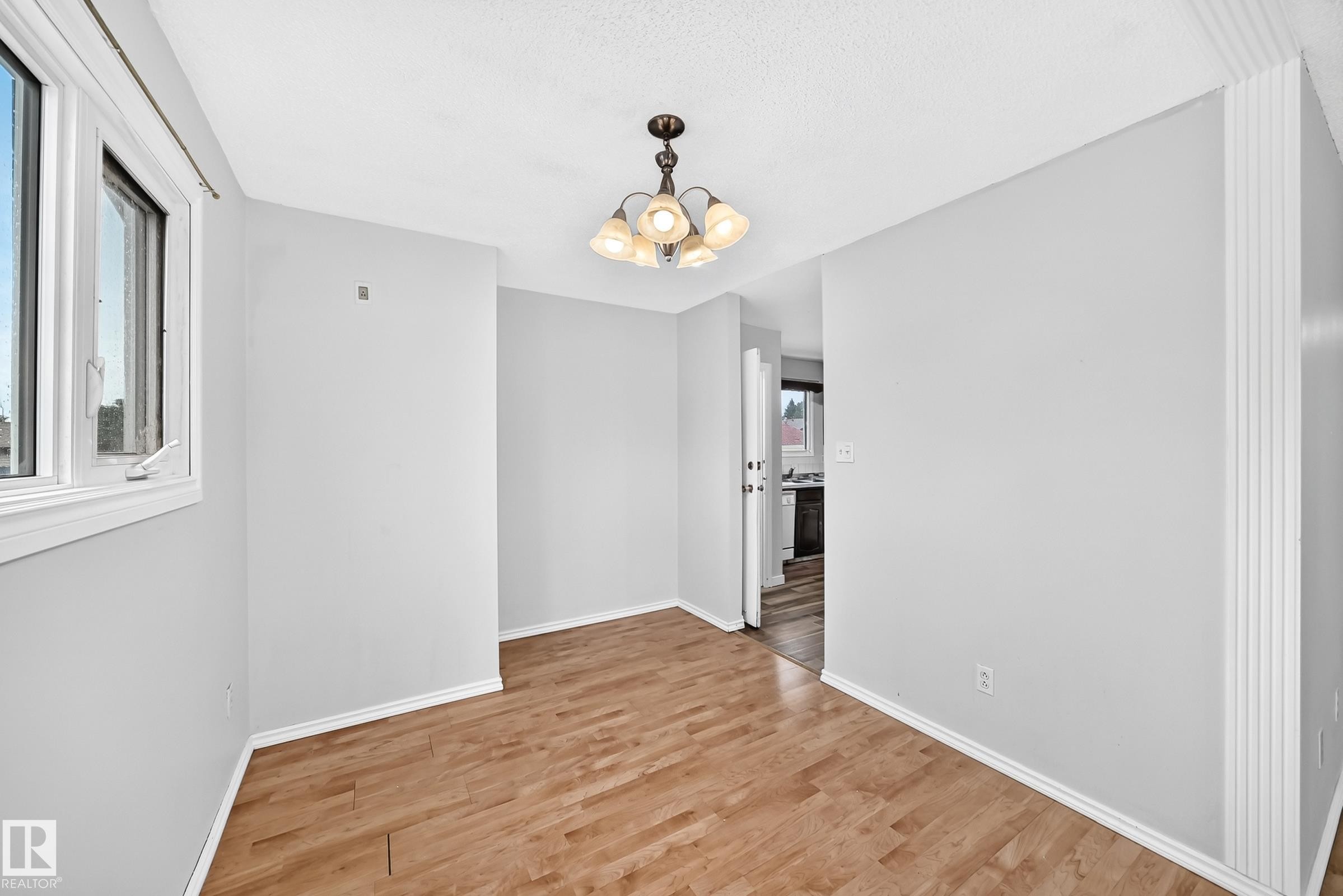 Open concept area featuring wood-finish flooring, white trim, and a multi-light chandelier - 1103 56 Street, Edmonton, AB
