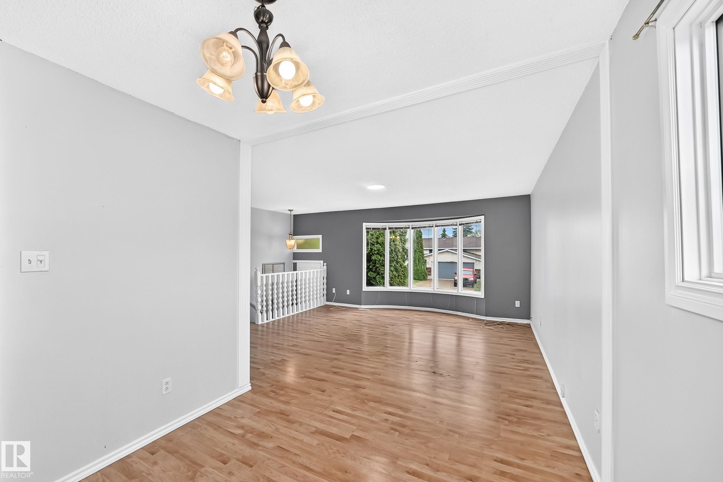 Spacious living area featuring wood-finish flooring, a decorative chandelier, and a large bay window - 1103 56 Street, Edmonton, AB