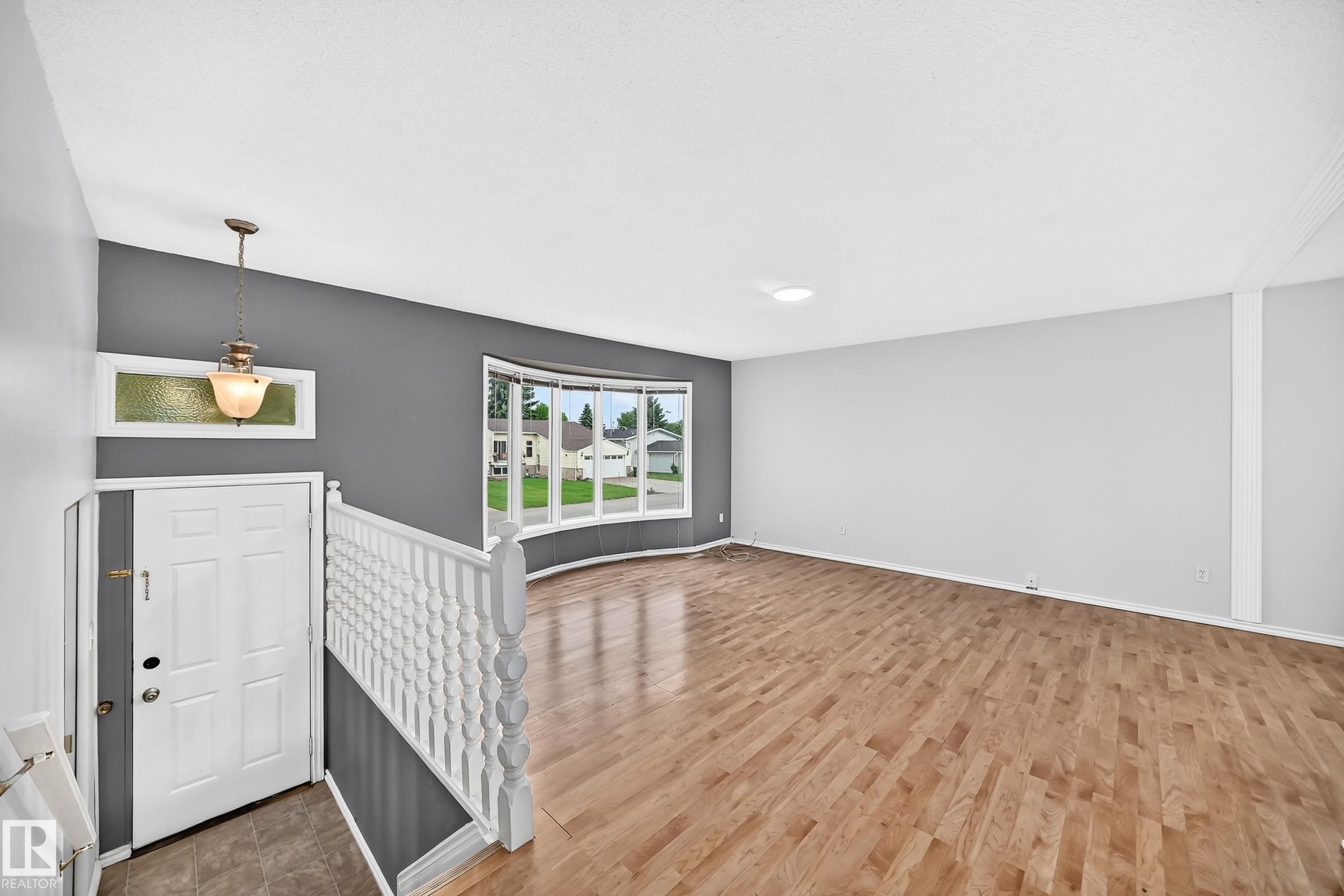 Spacious interior with wood-finish flooring, a curved bay window, and a white paneled entry door - 1103 56 Street, Edmonton, AB