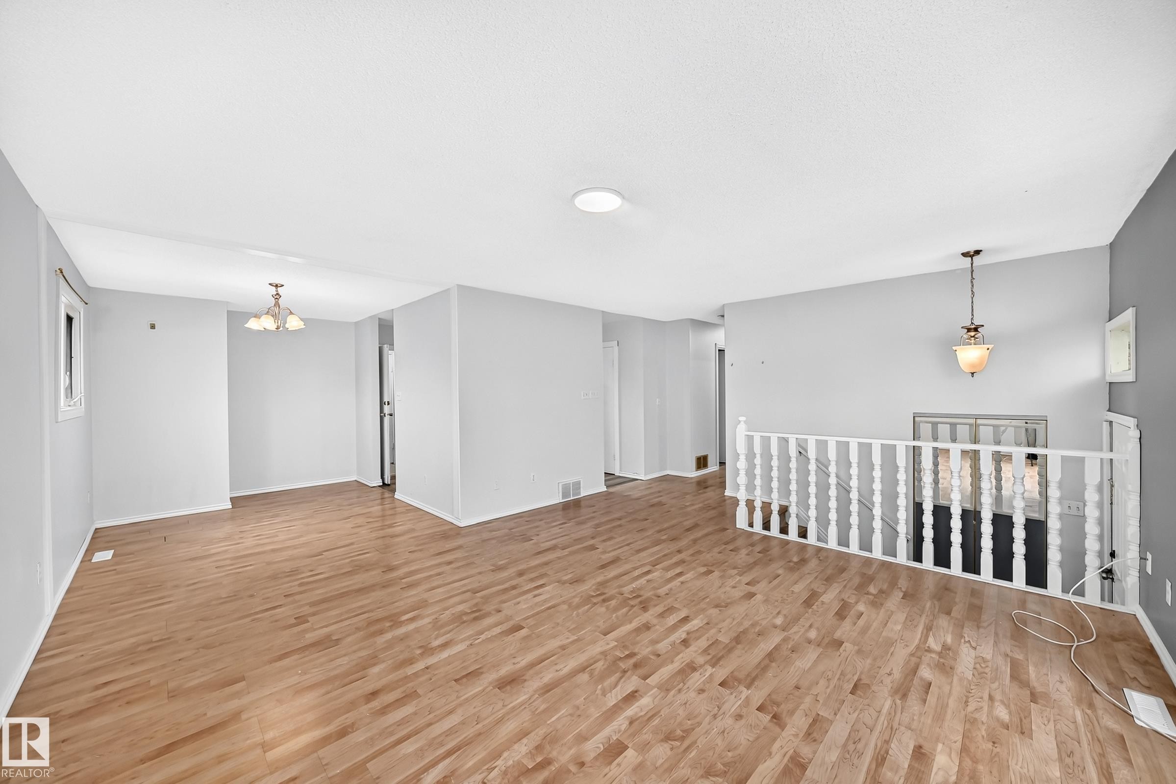 Expansive open-concept living space featuring wood-finish flooring, light gray wall tones, and a white spindle railing - 1103 56 Street, Edmonton, AB