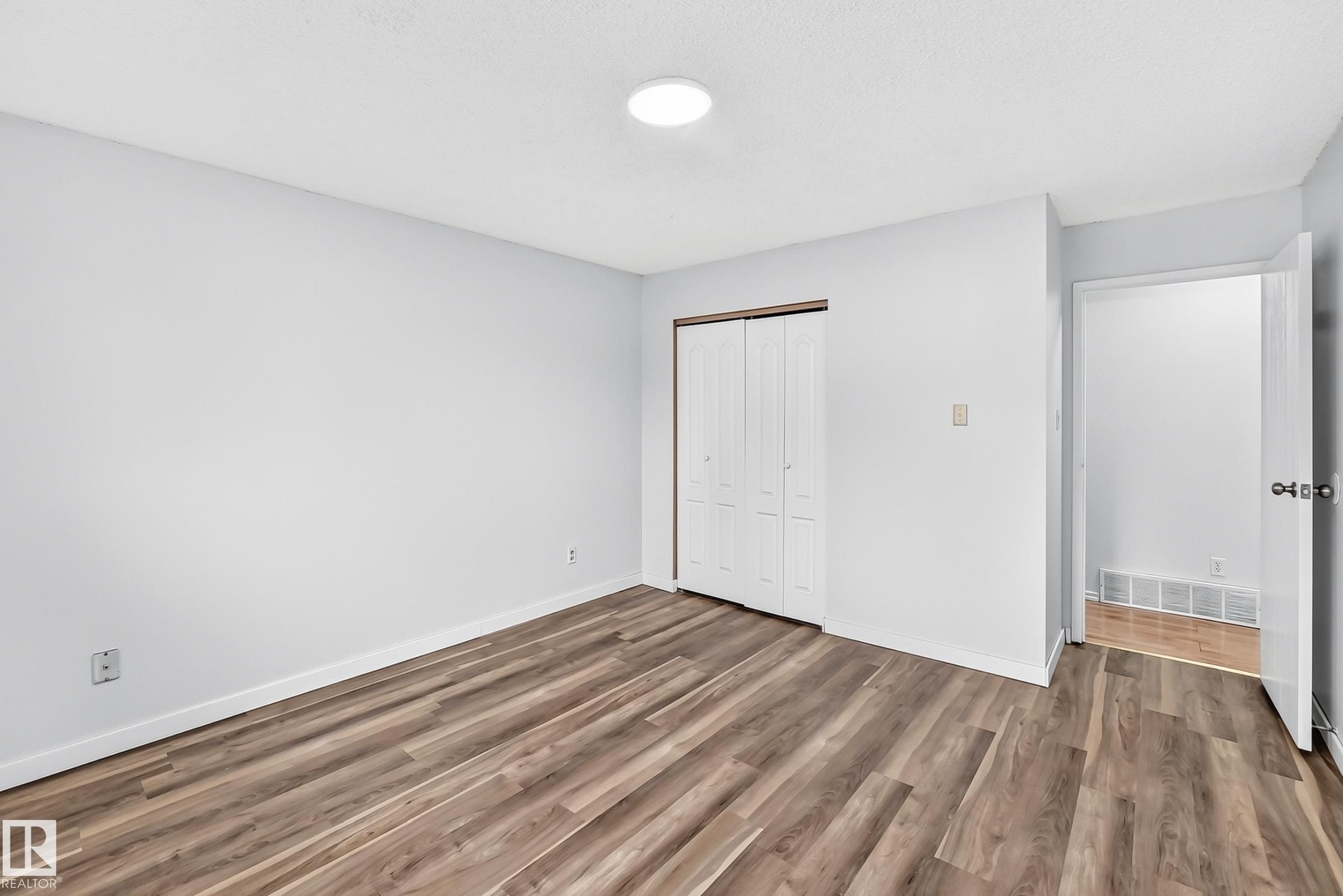 Room featuring wood-finish flooring, white baseboards, a ceiling-mounted light fixture, white walls, and a bi-fold closet door - 1103 56 Street, Edmonton, AB