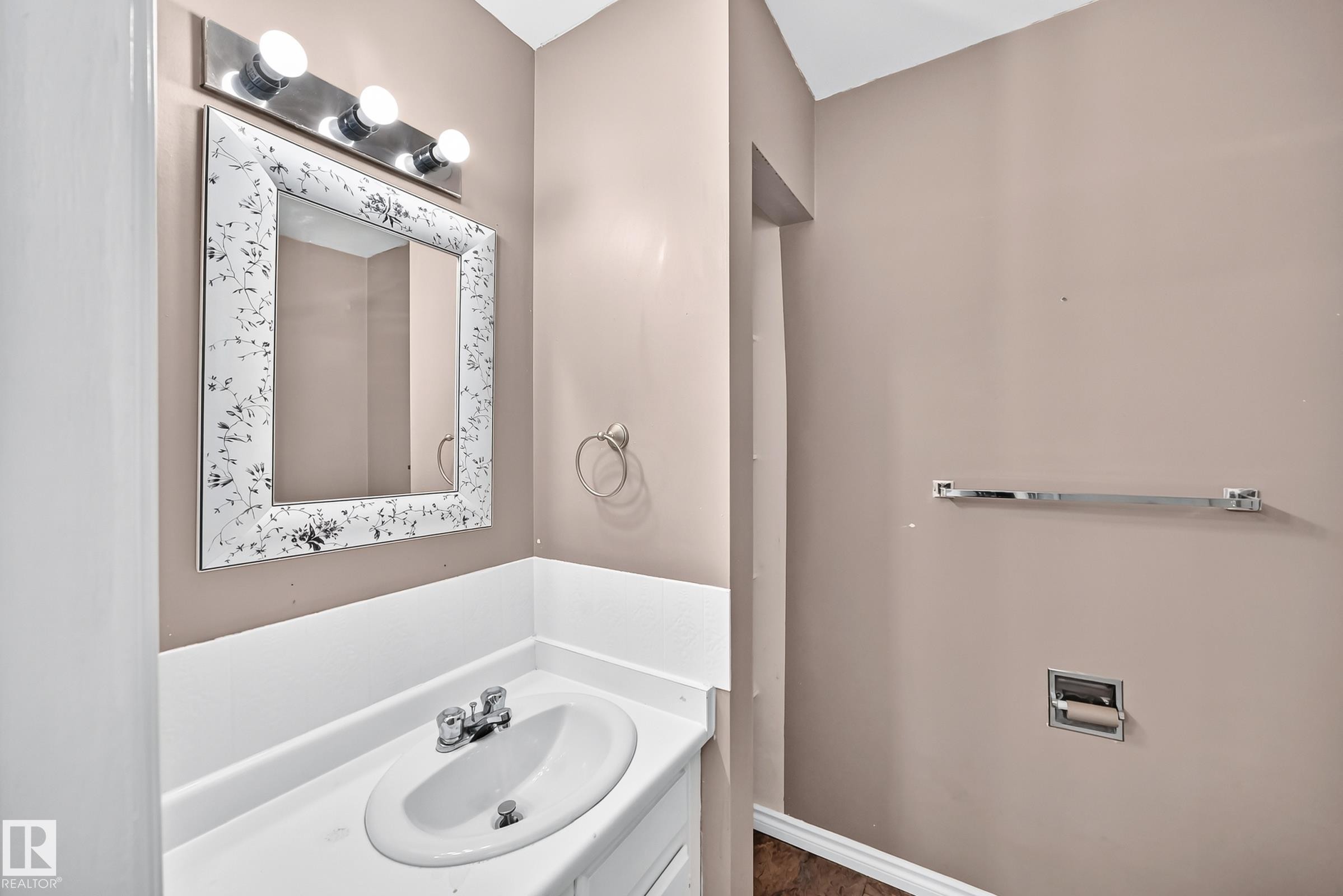 Bathroom vanity featuring an integrated sink, white countertop, and decorative framed mirror - 1103 56 Street, Edmonton, AB