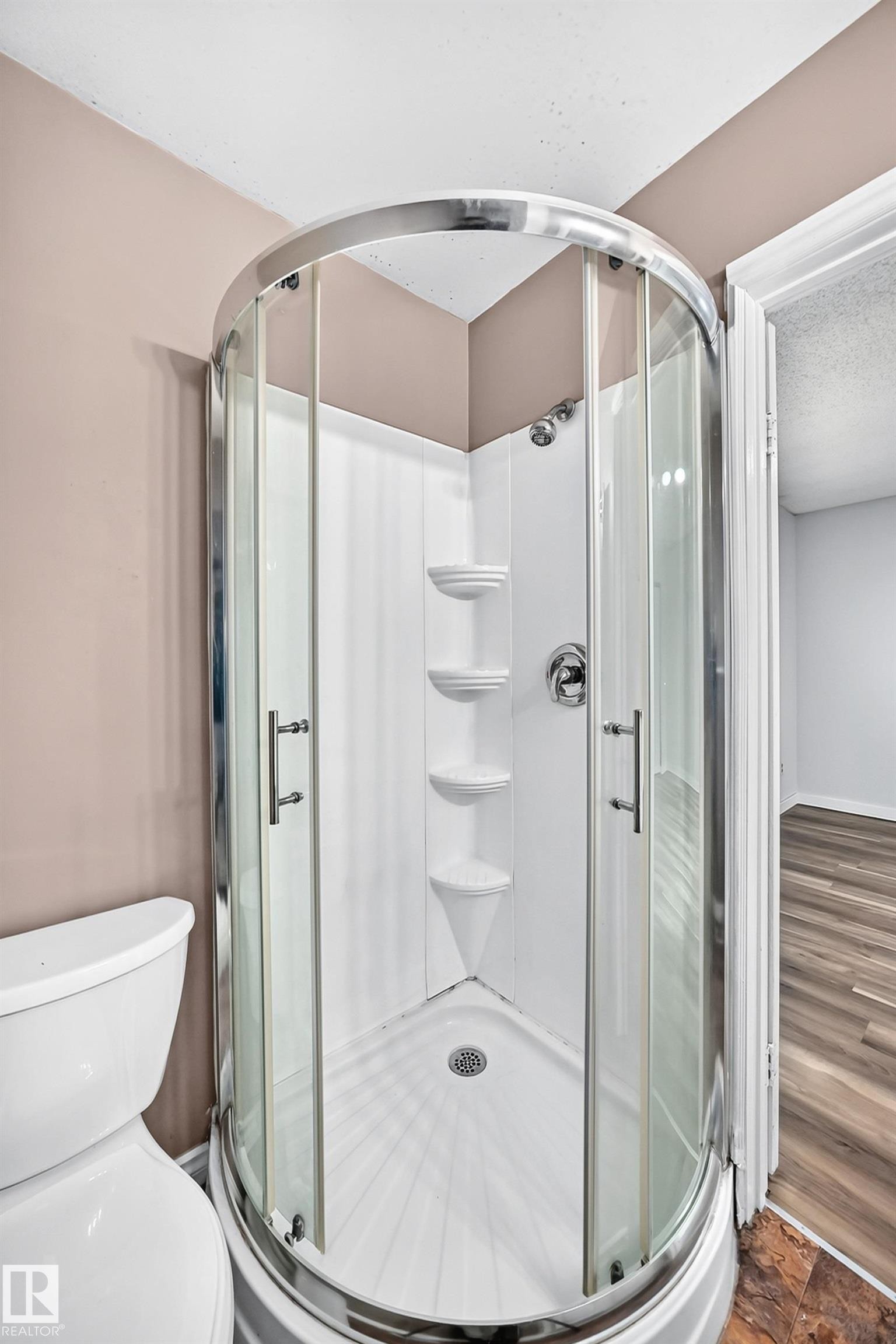 Corner shower enclosure with clear glass doors, chrome hardware, integrated shelving, and a white base - 1103 56 Street, Edmonton, AB