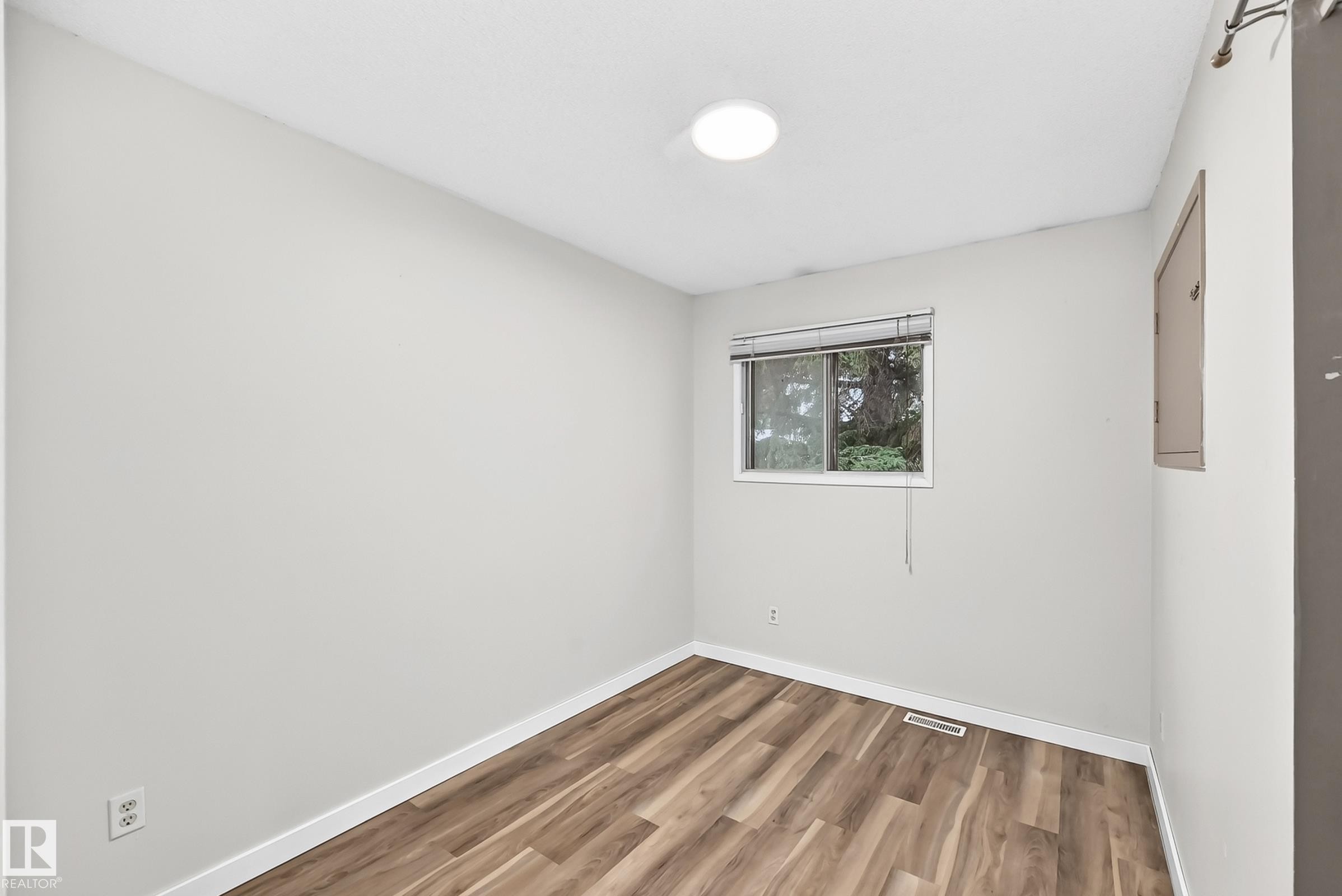 Bright room featuring light gray walls, wood-finish flooring, white trim, and a window with blinds - 1103 56 Street, Edmonton, AB