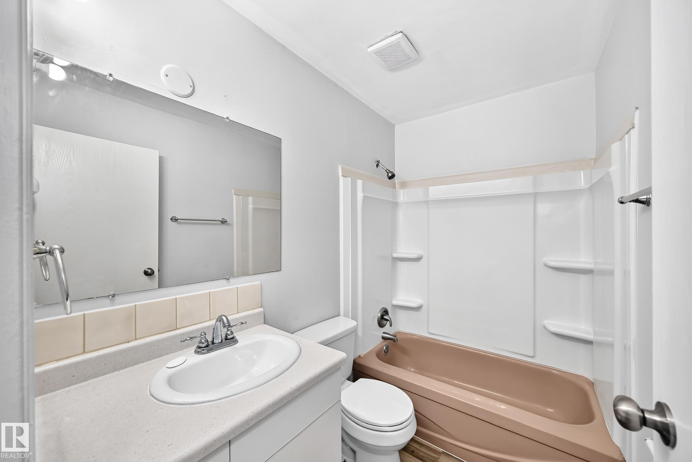 Bathroom featuring a built-in vanity with an integrated sink and chrome faucet, a mounted mirror, and a full bathtub with shower surround - 1103 56 Street, Edmonton, AB
