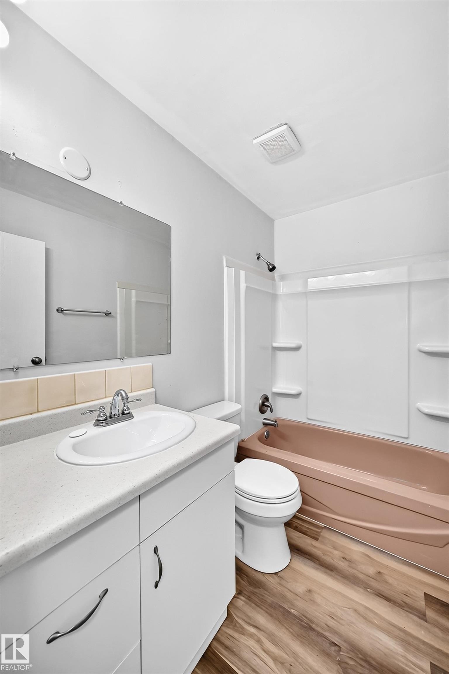 Bathroom featuring a vanity with a white countertop and base cabinetry, a drop-in sink with a chrome faucet, wood-finish flooring, and a shower/tub combination - 1103 56 Street, Edmonton, AB
