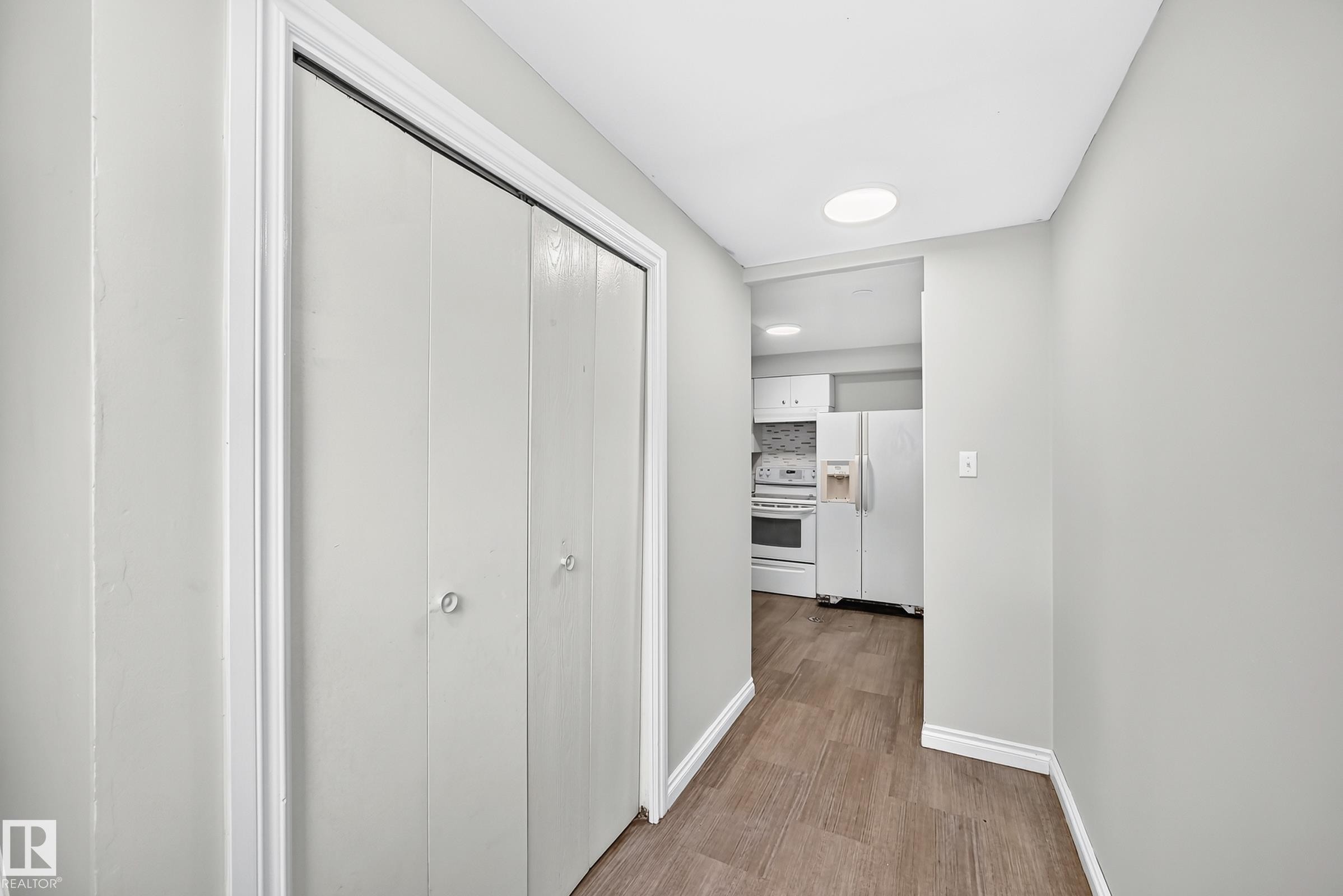 Hallway featuring wood-finish flooring, light gray walls, and white bi-fold doors - 1103 56 Street, Edmonton, AB
