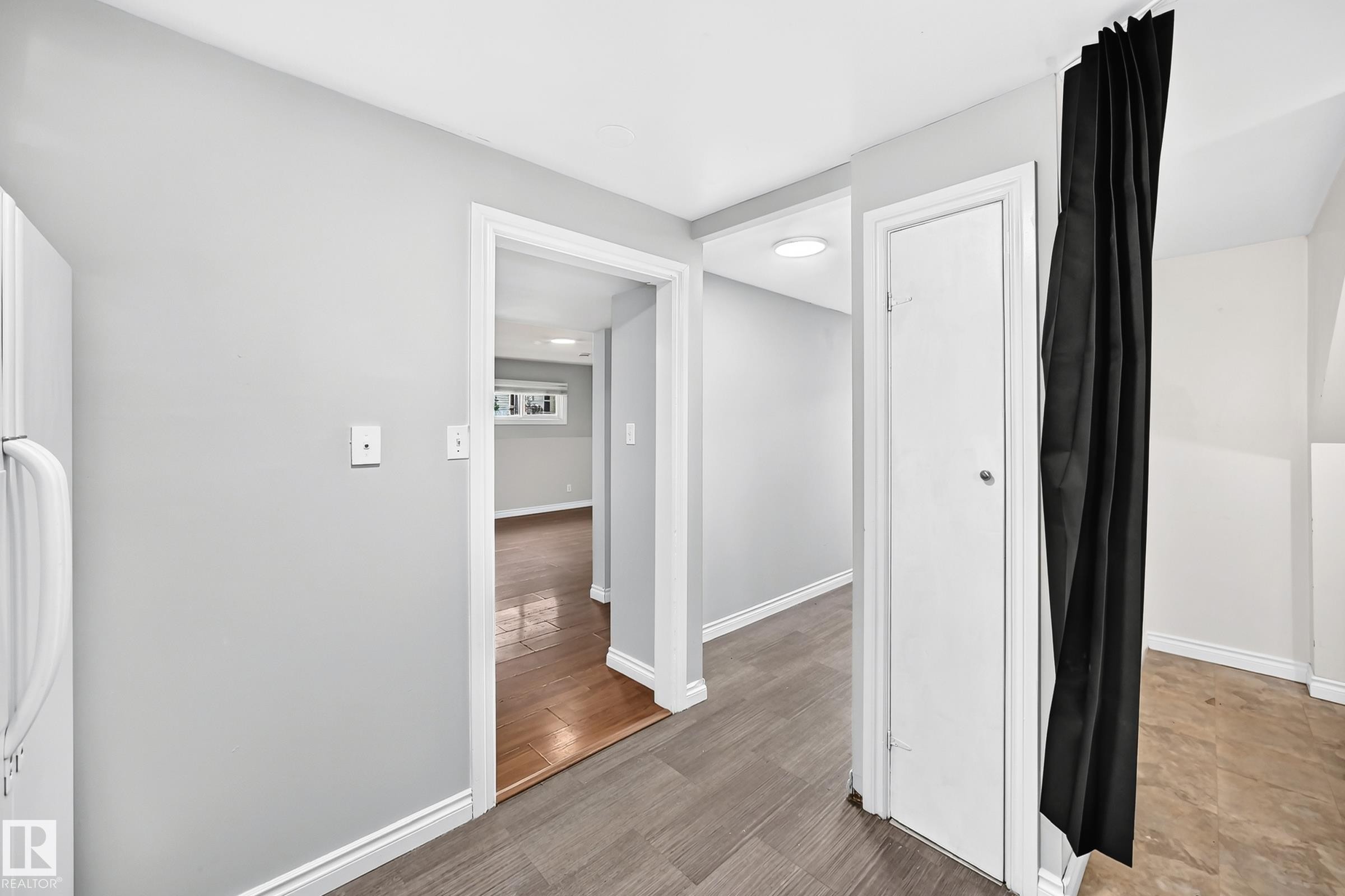 Interior hallway featuring wood-finish flooring, light gray wall paint, white baseboards, and a white interior door with a silver knob - 1103 56 Street, Edmonton, AB