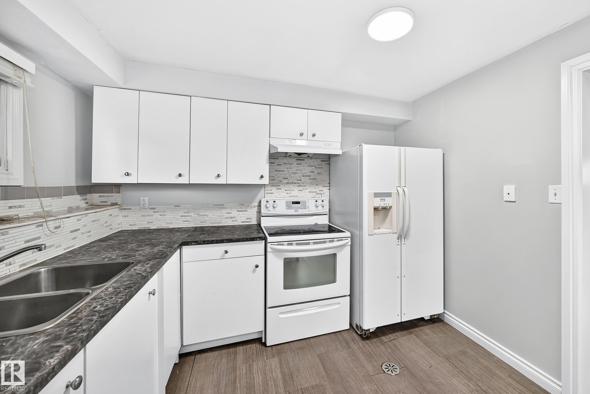 Modern kitchen featuring white cabinetry, a double basin stainless steel sink, patterned tile backsplash, and wood-finish flooring - 1103 56 Street, Edmonton, AB