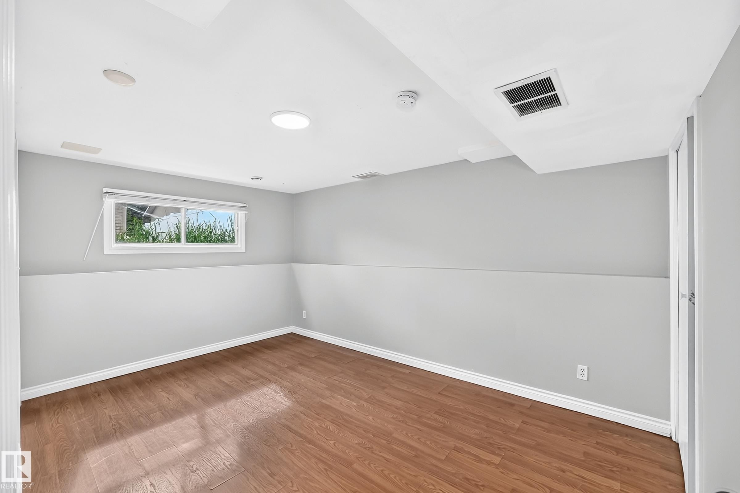 Spacious room featuring wood-finish flooring, a window with exterior greenery, recessed lighting, and a white ceiling - 1103 56 Street, Edmonton, AB