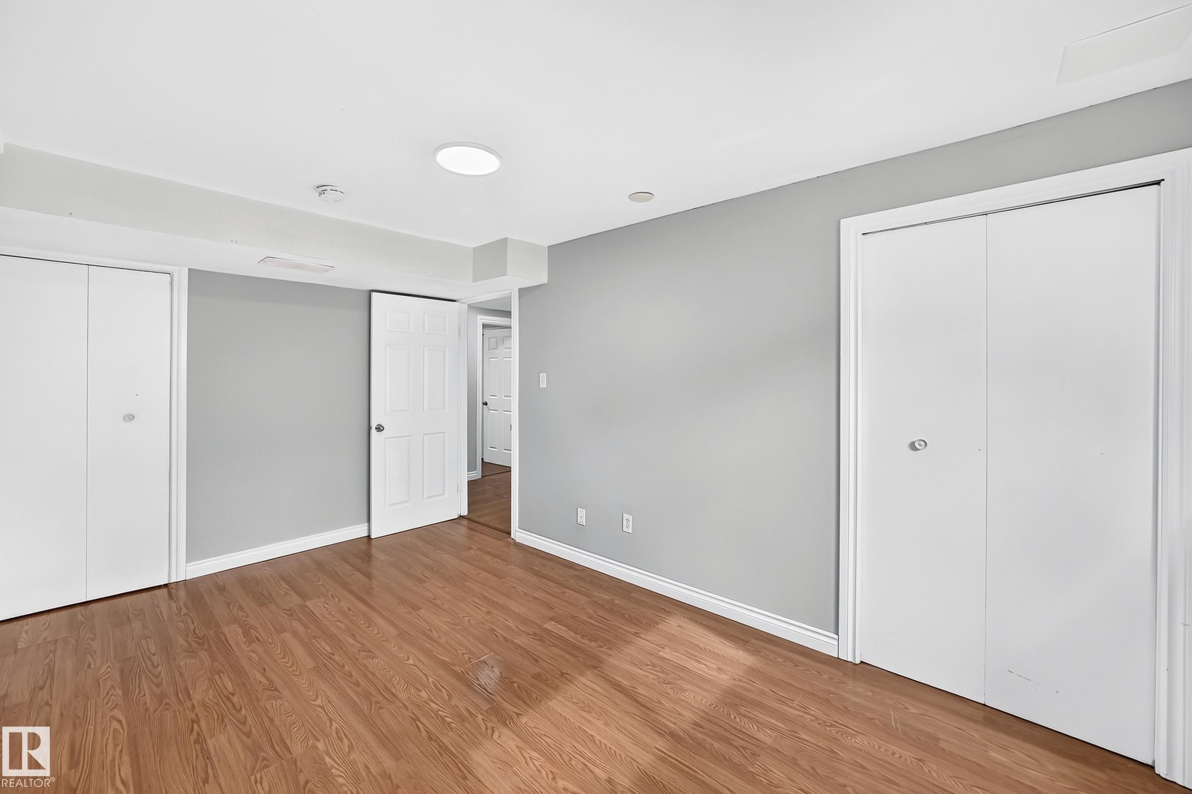 Spacious room featuring wood-finish flooring, light gray wall paint, and white trim - 1103 56 Street, Edmonton, AB