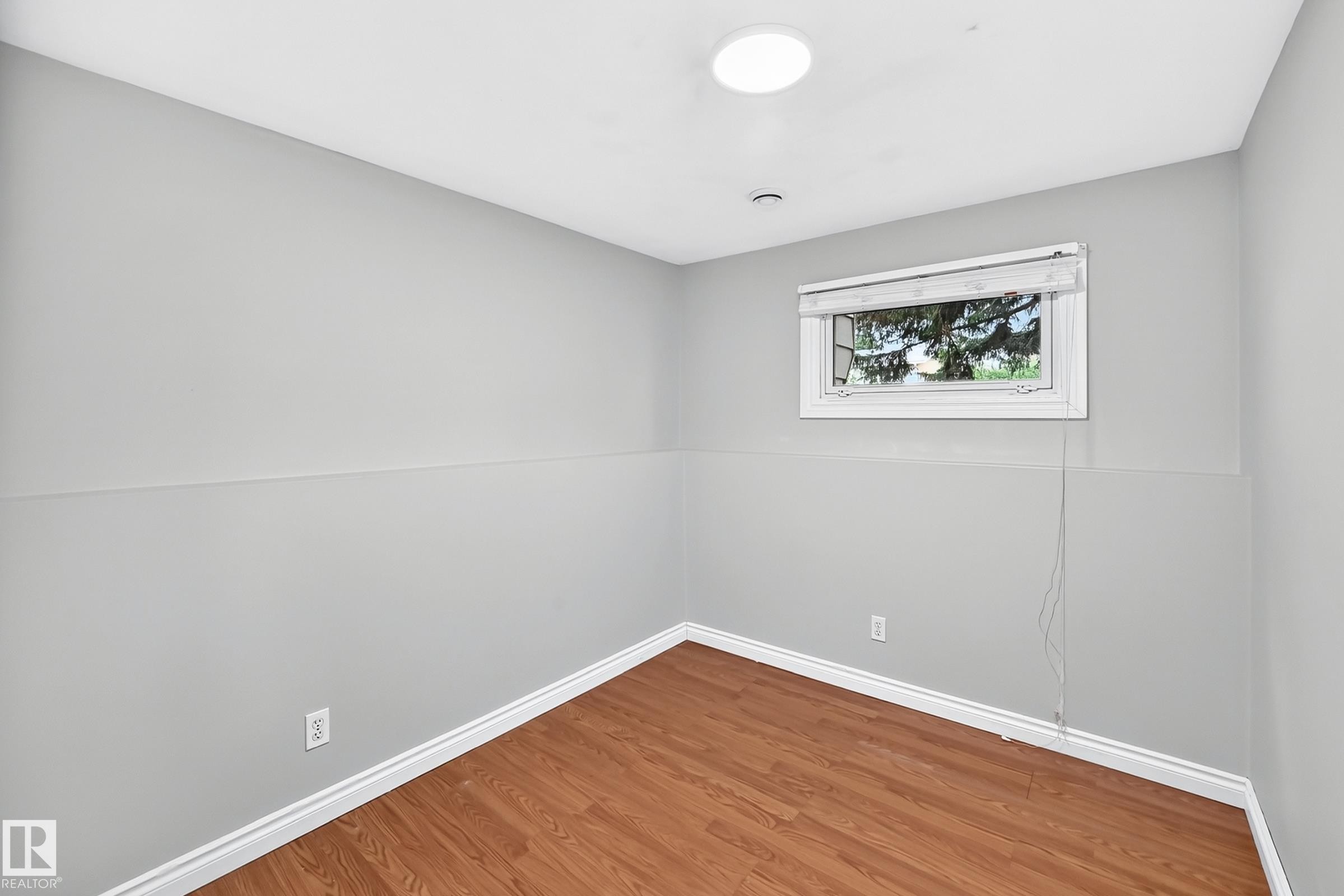 Interior room featuring light gray walls, white baseboards, wood-finish flooring, and a large window with white trim - 1103 56 Street, Edmonton, AB