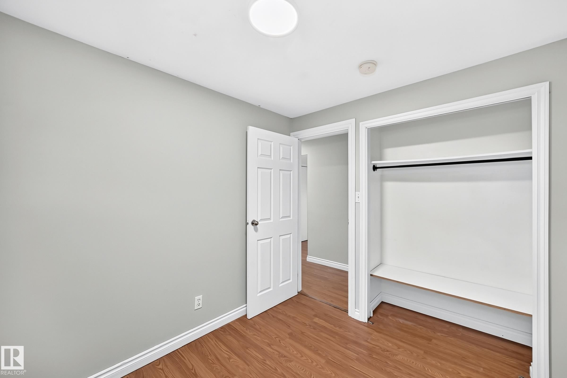 Interior room featuring light gray walls, wood-finish flooring, white baseboards, and a flush-mount ceiling light - 1103 56 Street, Edmonton, AB