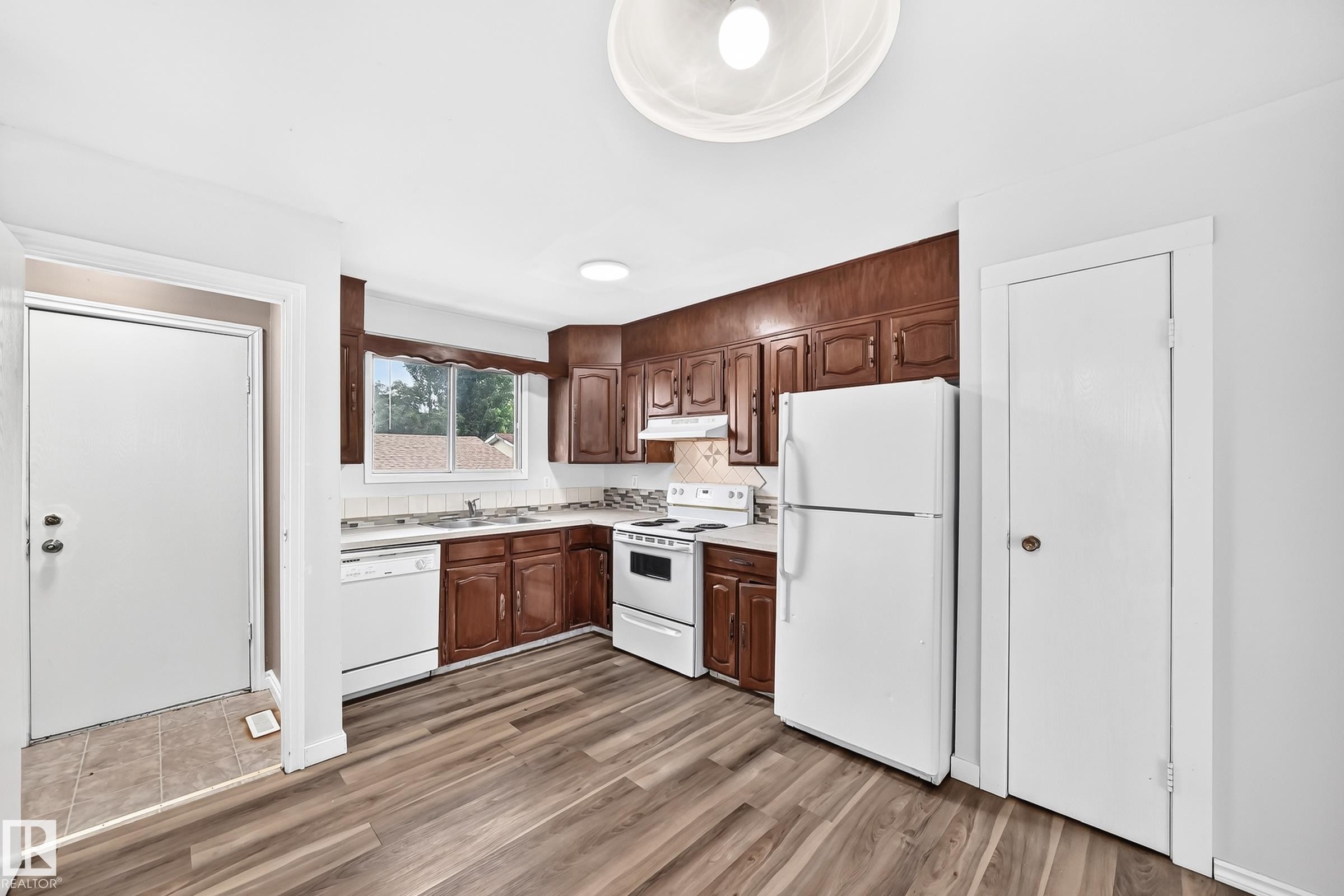 Kitchen featuring wood-finish flooring, wood cabinetry, white appliances, and a tiled backsplash - 1103 56 Street, Edmonton, AB