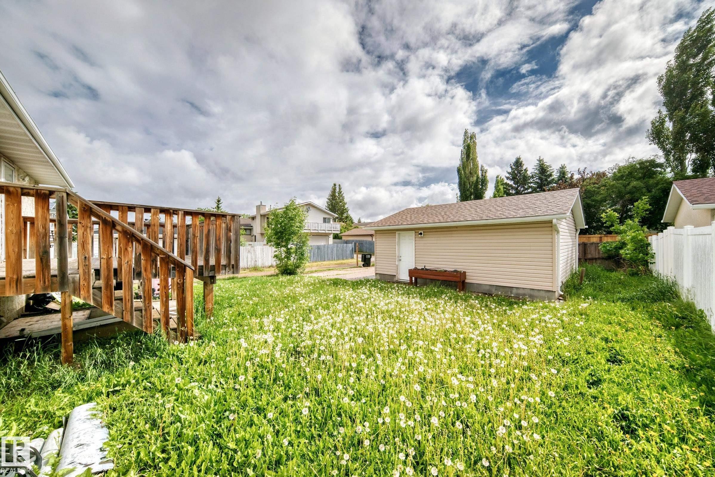 Expansive backyard featuring a wood deck with railings, a detached garage with beige siding and a shingle roof, and a white picket fence bordering the property - 1103 56 Street, Edmonton, AB