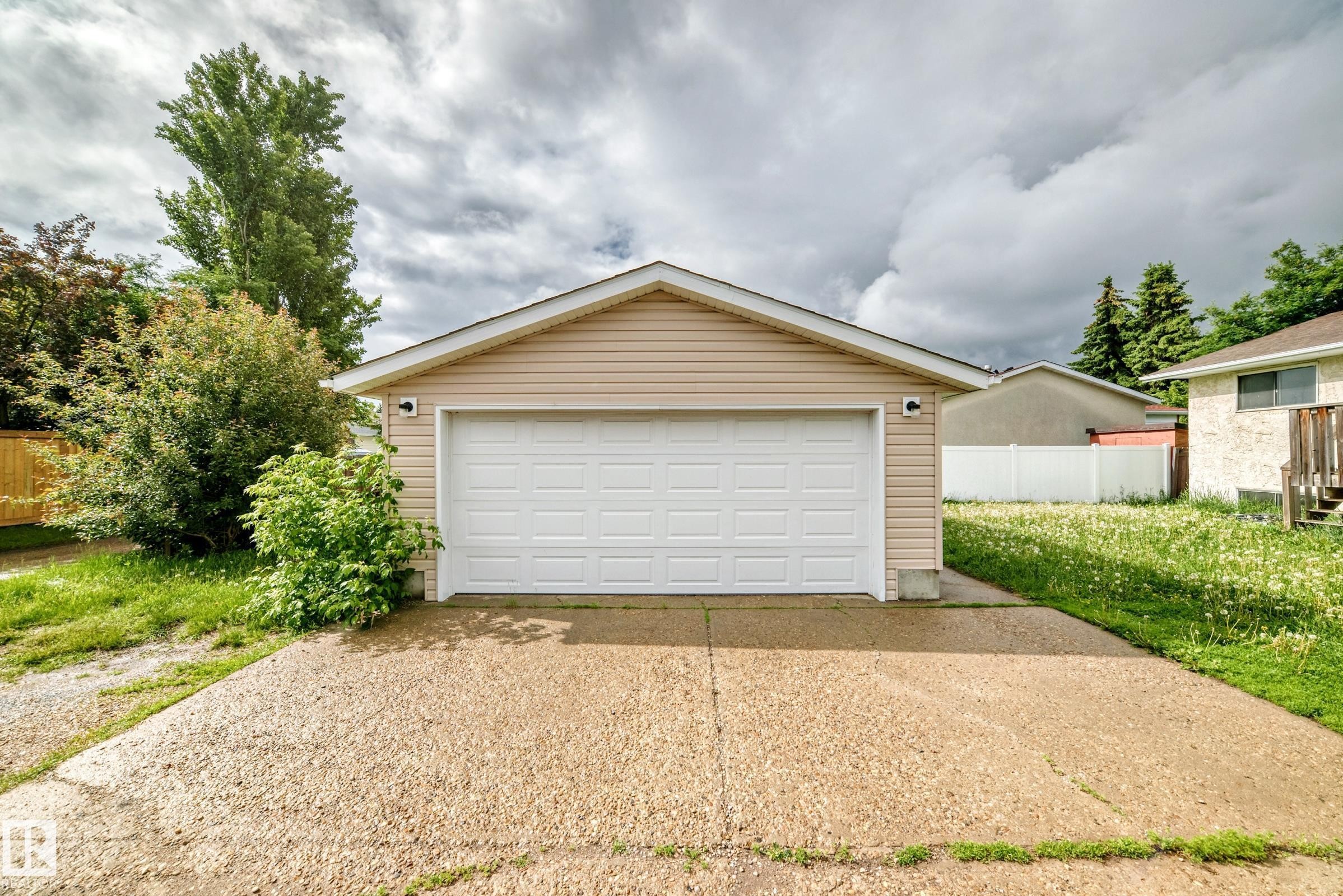 Detached garage with tan siding, a white panel garage door, and a concrete driveway - 1103 56 Street, Edmonton, AB