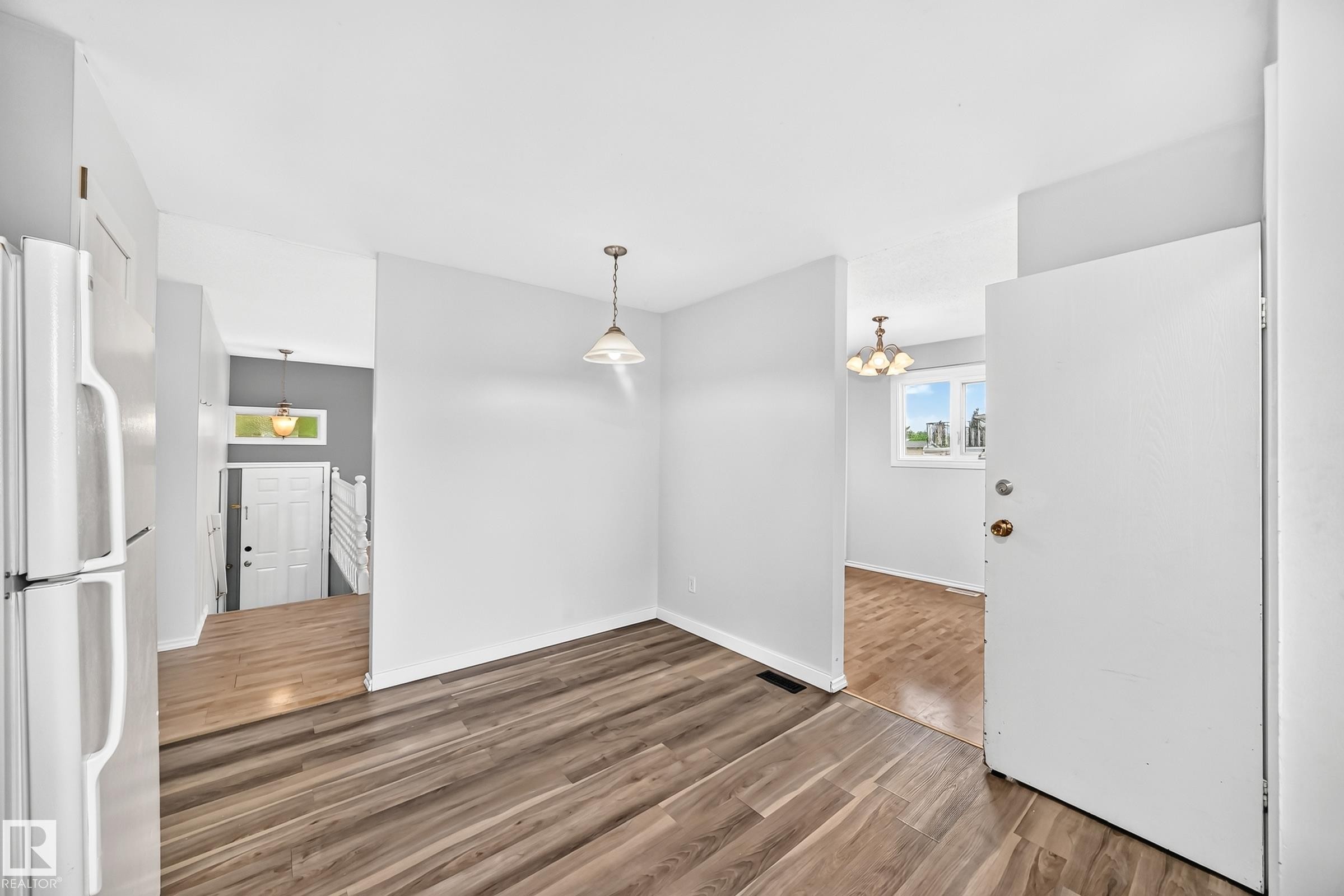 Wood-finish flooring throughout, featuring a white entry door with brass hardware, a pendant light fixture, and white painted walls - 1103 56 Street, Edmonton, AB