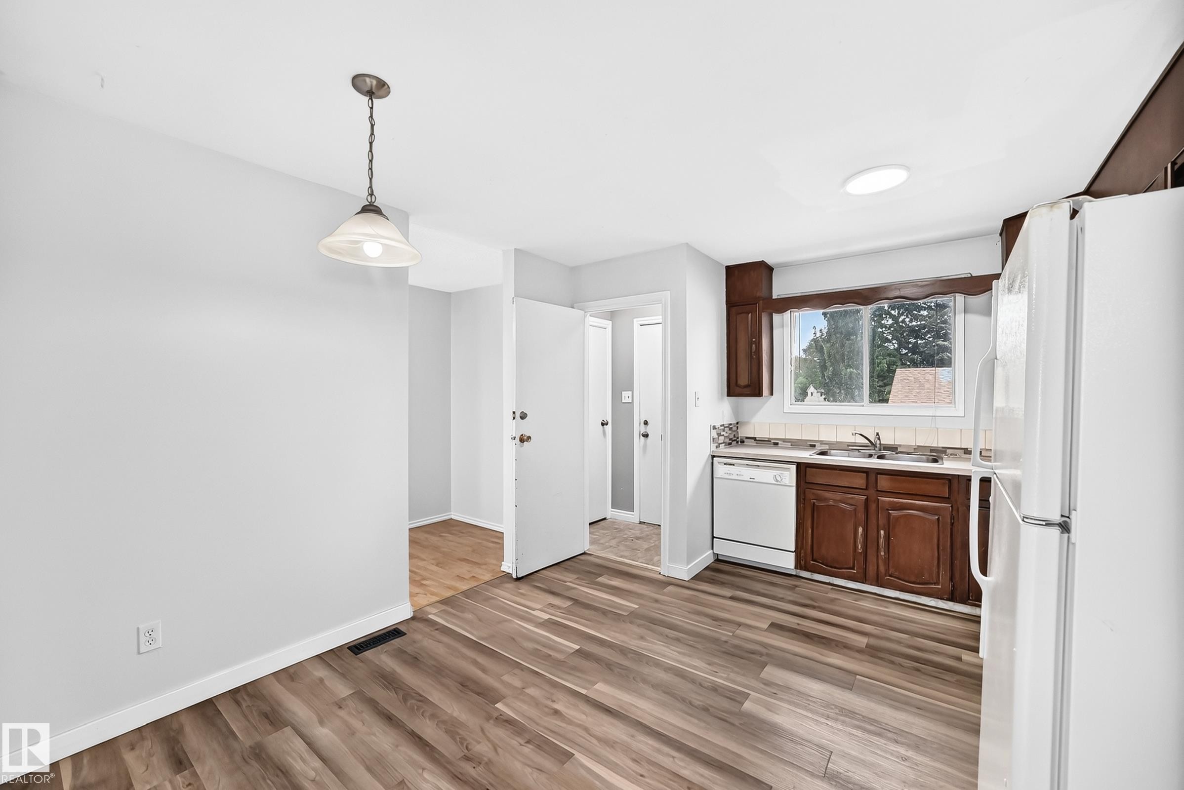 Kitchen featuring wood-finish flooring, dark wood cabinetry, a white tile backsplash, and a window above the sink - 1103 56 Street, Edmonton, AB