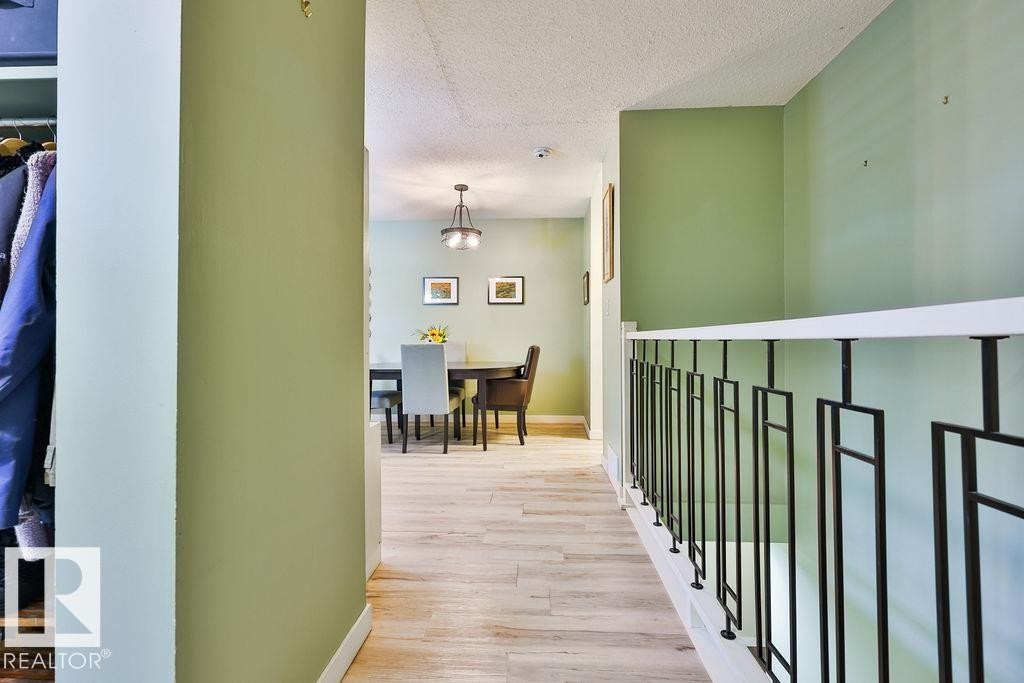Hallway featuring wood-finish flooring, a modern black metal and white railing, and light green wall paint - 17009 109 Street, Edmonton, AB