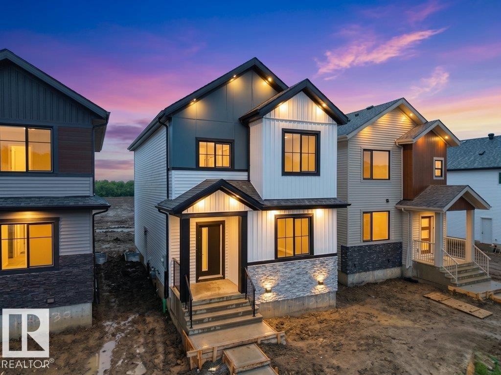Modern architectural design featuring prominent gables, mixed-material siding including board and batten, stone veneer accents, and dark-framed windows - 18719 130 Street Nw, Edmonton, AB