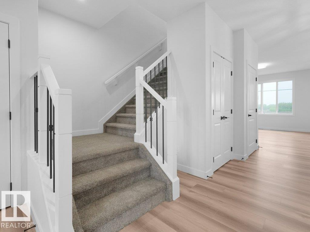 Carpeted staircase featuring white newel posts and black iron balusters - 18719 130 Street Nw, Edmonton, AB