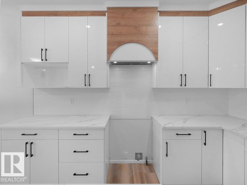 Modern kitchen featuring white cabinetry with matte black hardware, stone countertops, a subway tile backsplash, and wood-finish flooring - 18719 130 Street Nw, Edmonton, AB