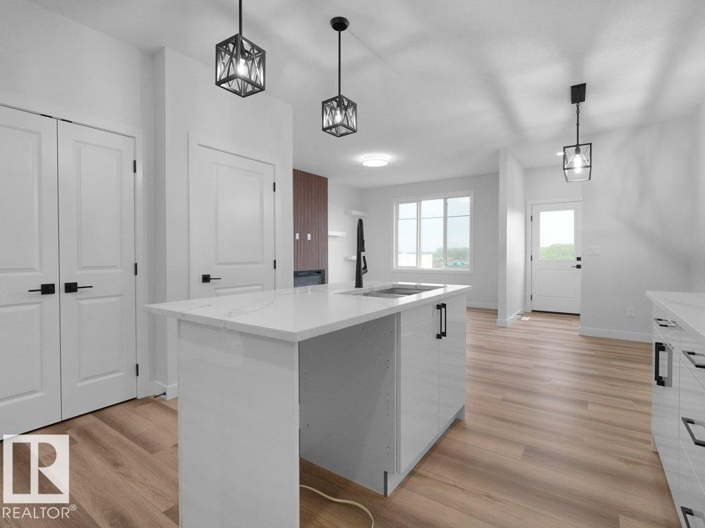 Modern kitchen island featuring a white quartz countertop, integrated sink, and black faucet - 18719 130 Street Nw, Edmonton, AB