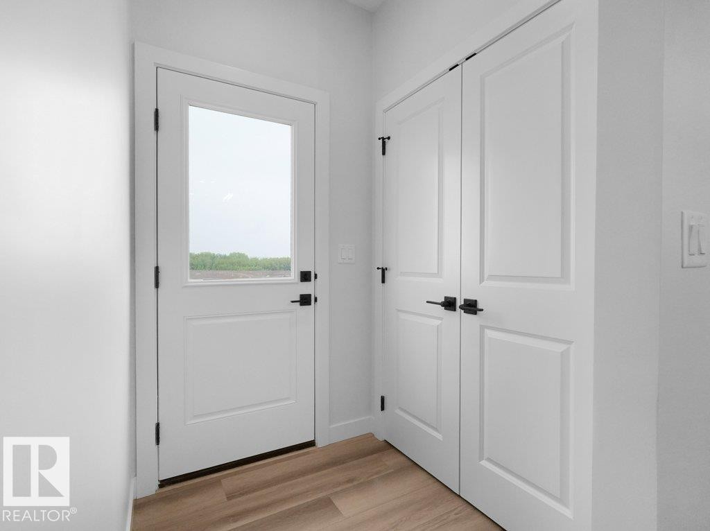 Entryway featuring a white door with transom-style glass, matte black hardware, and wood-finish flooring - 18719 130 Street Nw, Edmonton, AB