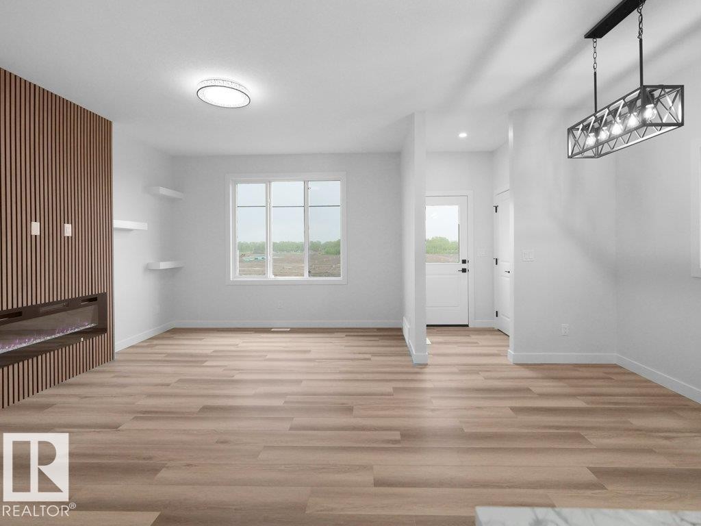 Spacious living area featuring light wood-finish flooring, a contemporary linear electric fireplace with a slatted wood accent wall, and a large window providing ample natural light - 18719 130 Street Nw, Edmonton, AB