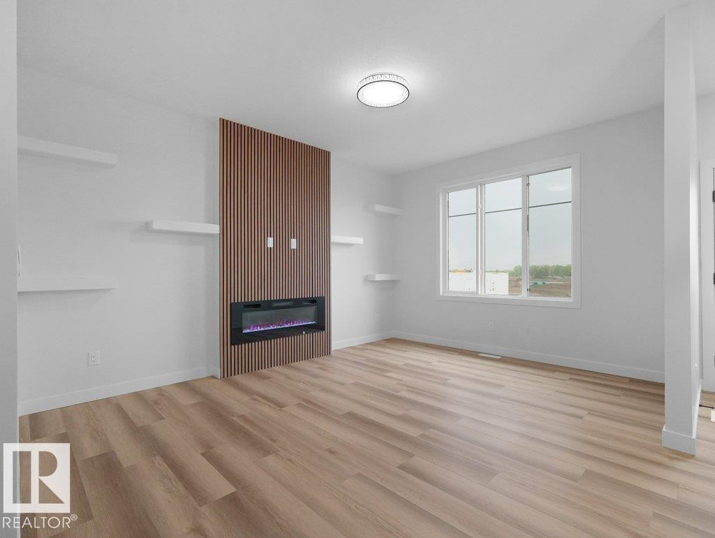 Open-concept living space with wood-finish flooring, a contemporary electric fireplace with wood slat accent, multiple wall-mounted shelves, and a large window - 18719 130 Street Nw, Edmonton, AB
