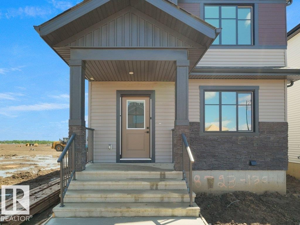 Front exterior featuring a covered entry, stone veneer accents, multi-pane windows, and a panel door with an upper glass insert - 18719 130 Street Nw, Edmonton, AB