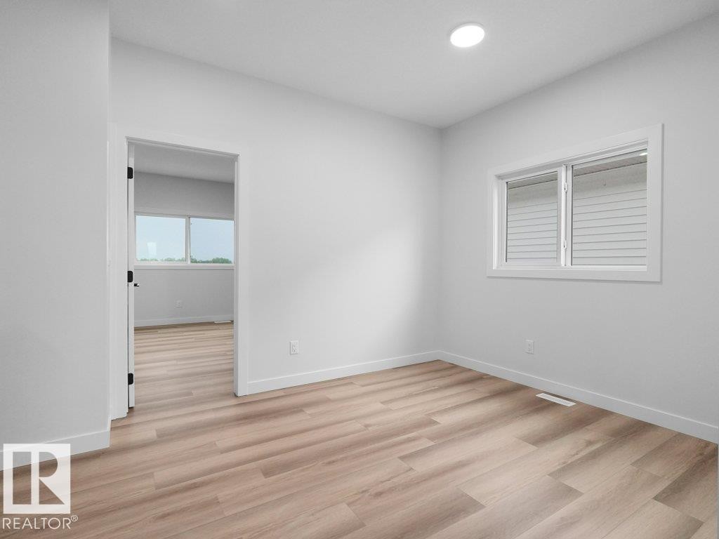Spacious room featuring wood-finish flooring, white baseboards, and a recessed ceiling light - 18719 130 Street Nw, Edmonton, AB