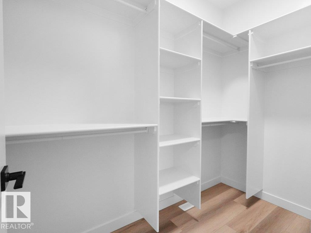 Walk-in closet featuring white built-in shelving, multiple hanging rods, and wood-finish flooring - 18719 130 Street Nw, Edmonton, AB