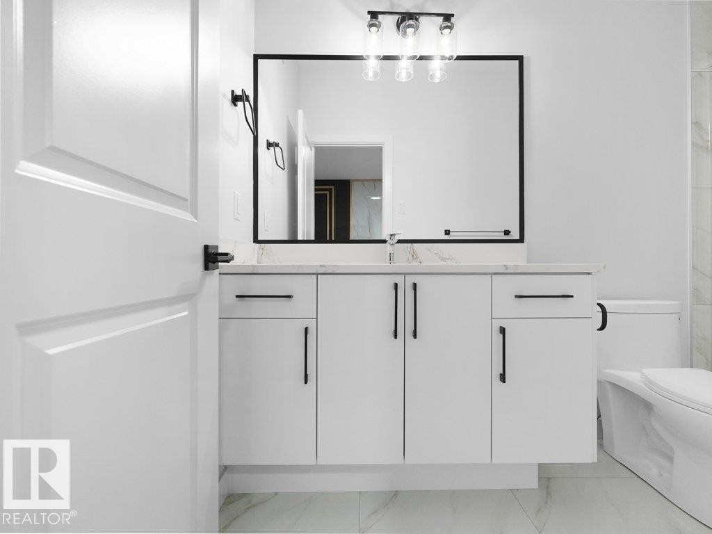 Contemporary bathroom vanity featuring white cabinetry, a light-toned countertop, and a large framed mirror - 18719 130 Street Nw, Edmonton, AB