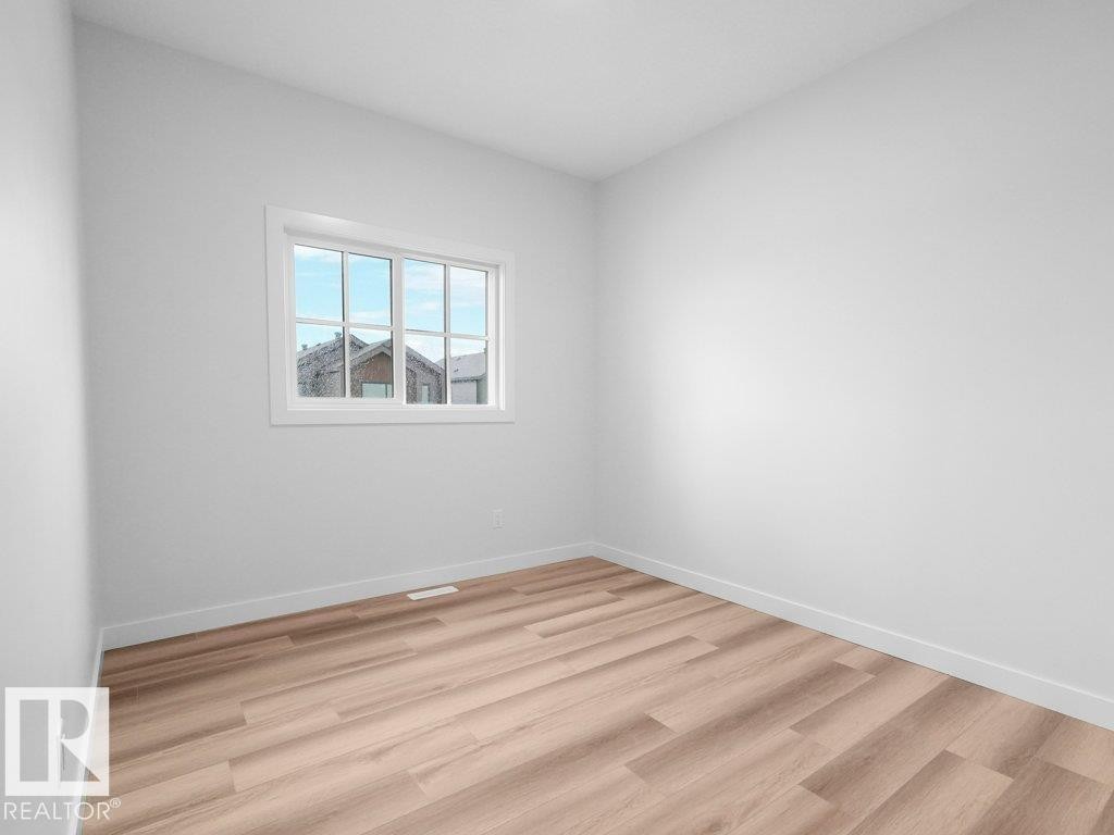 Room featuring light wood-finish flooring, white baseboards, and a white-framed window - 18719 130 Street Nw, Edmonton, AB