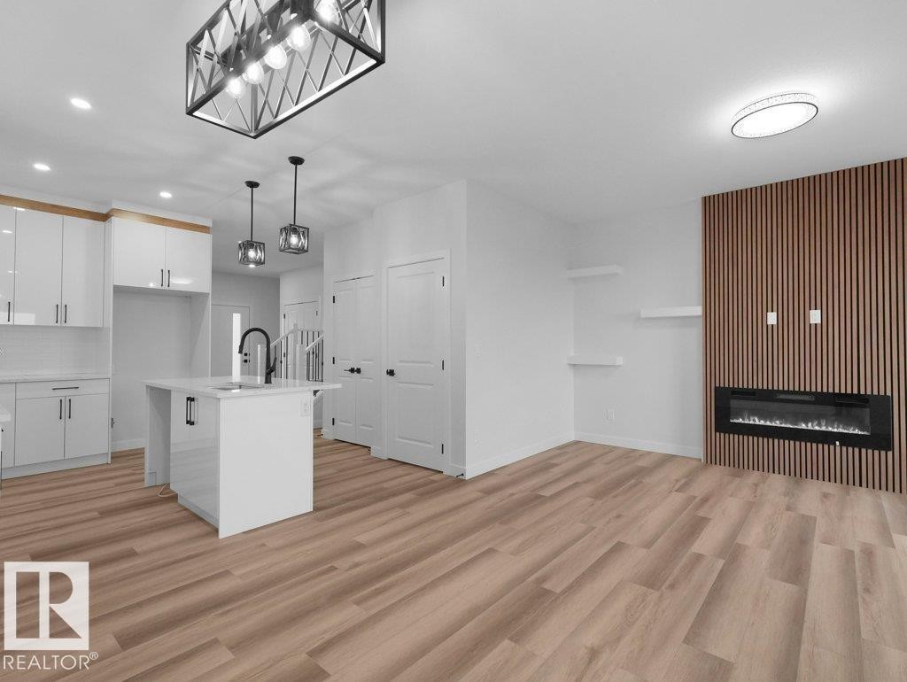Open-concept living space with wood-finish flooring, a contemporary kitchen island with a built-in sink, and a feature wall with an electric fireplace - 18719 130 Street Nw, Edmonton, AB