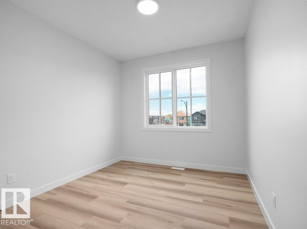 Bright interior space featuring a multi-pane window, wood-finish flooring, white baseboards, and a flush-mount ceiling light - 18719 130 Street Nw, Edmonton, AB