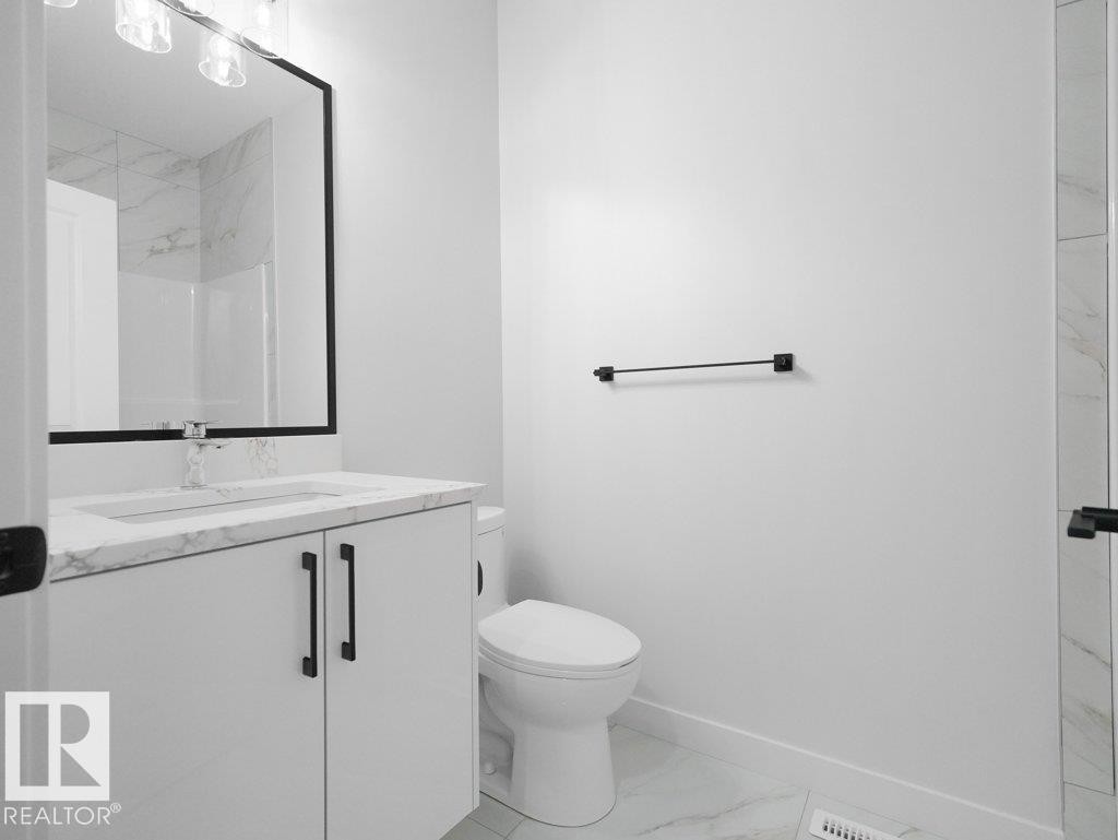Bathroom featuring a white vanity with a stone-finish countertop, integrated sink, and black hardware - 18719 130 Street Nw, Edmonton, AB