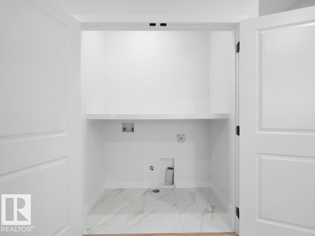 Dedicated laundry closet featuring white paneled double doors, interior shelving, and marble-look tile flooring - 18719 130 Street Nw, Edmonton, AB