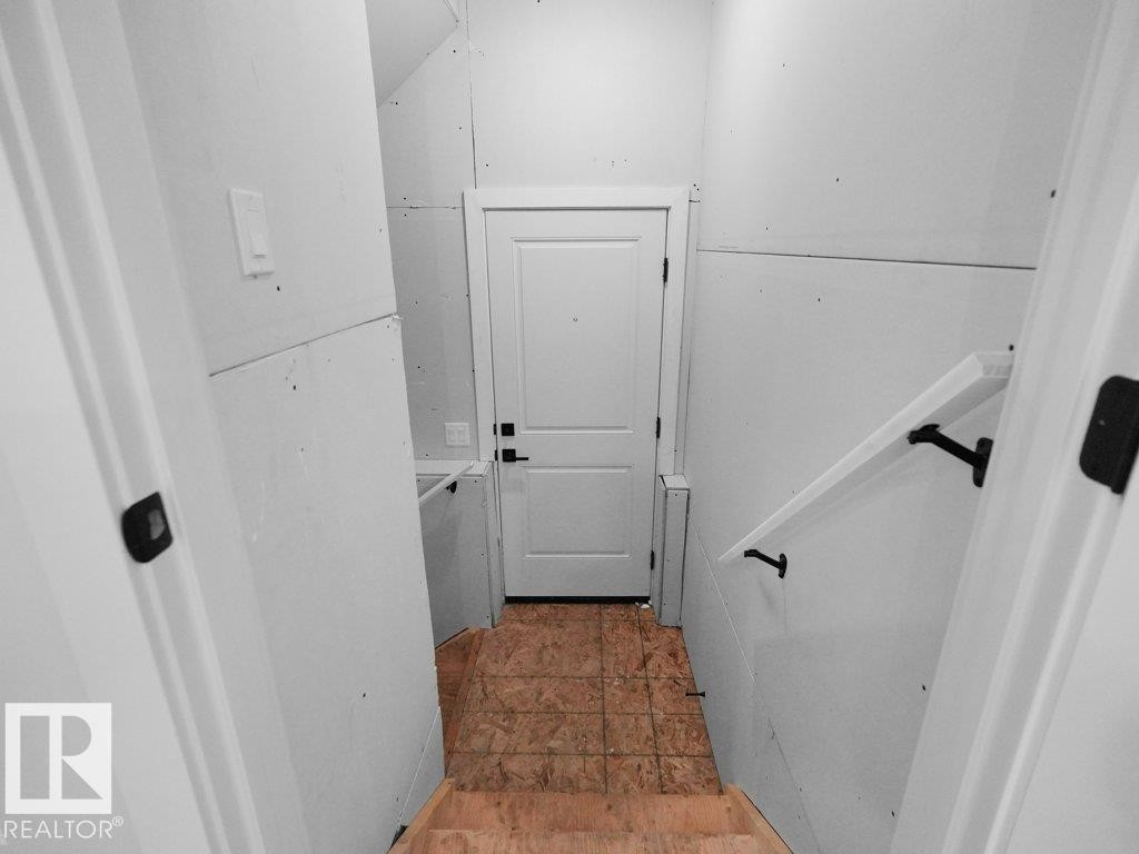 Unfinished interior entryway with a solid white door featuring black hardware, a light switch, and a white handrail with black brackets - 18719 130 Street Nw, Edmonton, AB