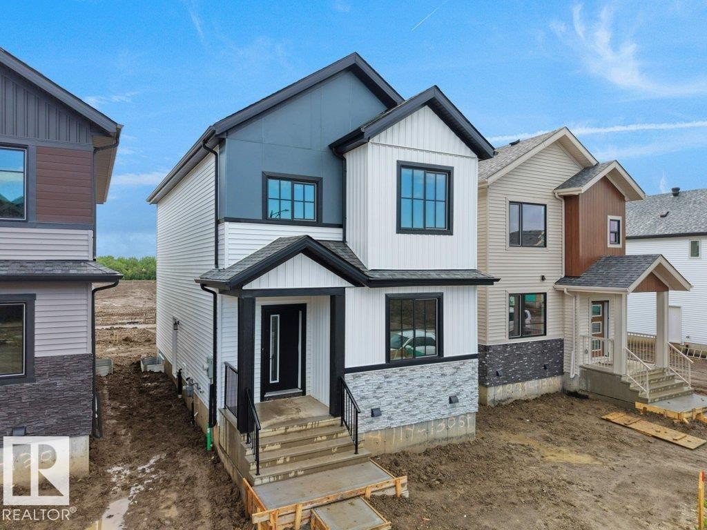 Contemporary two-story exterior featuring a prominent black main door, multi-pane black-framed windows, a combination of horizontal siding and vertical paneling, a stone veneer foundation accent, and a covered entry with black railings - 18719 130 Street Nw, Edmonton, AB