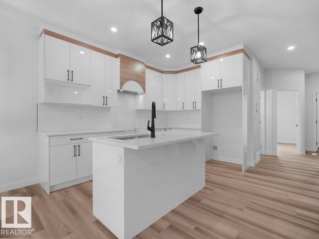 Modern kitchen featuring high-gloss white cabinetry with wood-finish accents, a central island with an integrated sink, and wood-finish flooring - 18719 130 Street Nw, Edmonton, AB
