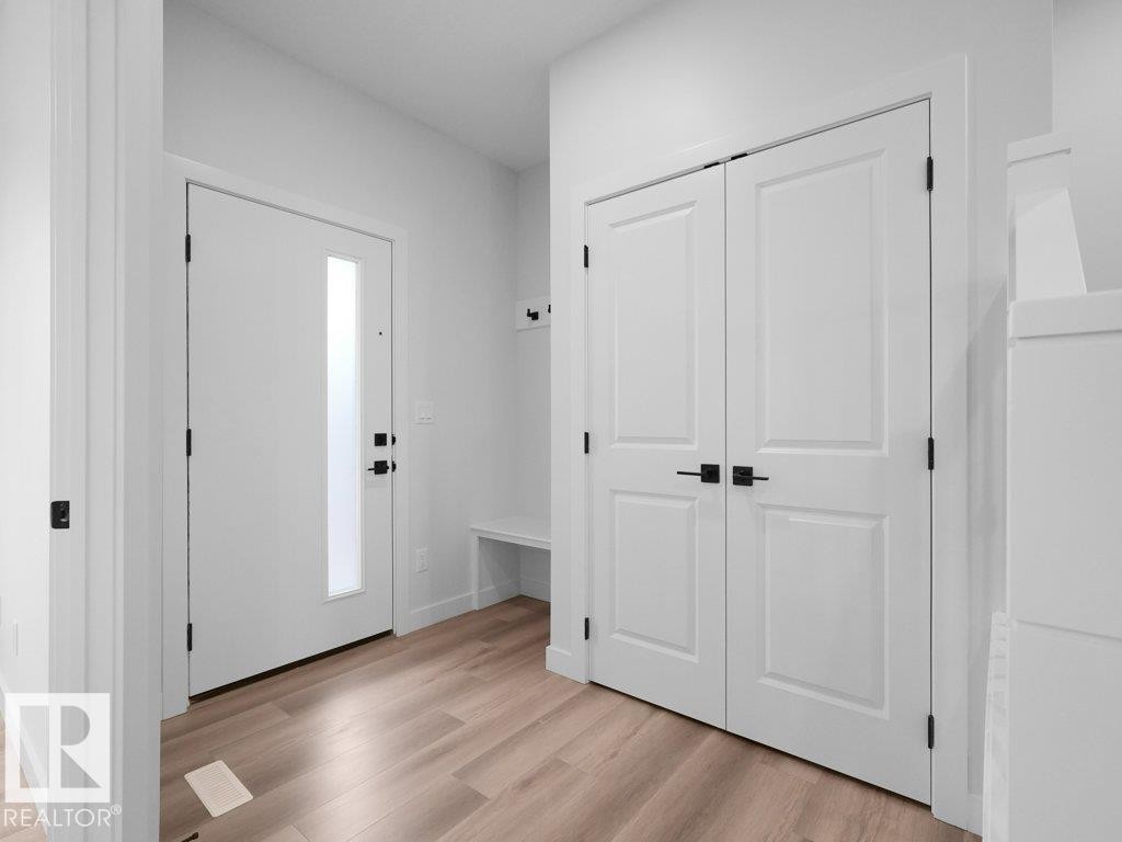 Entryway featuring a contemporary front door with frosted glass panel, wood-finish flooring, and a built-in bench with coat hooks - 18719 130 Street Nw, Edmonton, AB
