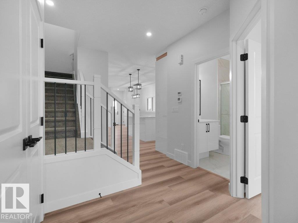 Entryway featuring wood-finish flooring, white walls, and a staircase with carpeted treads and black metal balusters - 18719 130 Street Nw, Edmonton, AB