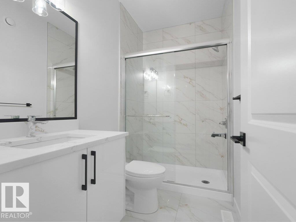 Bathroom featuring a white vanity with a light-toned countertop, a frameless mirror, and modern lighting fixtures - 18719 130 Street Nw, Edmonton, AB