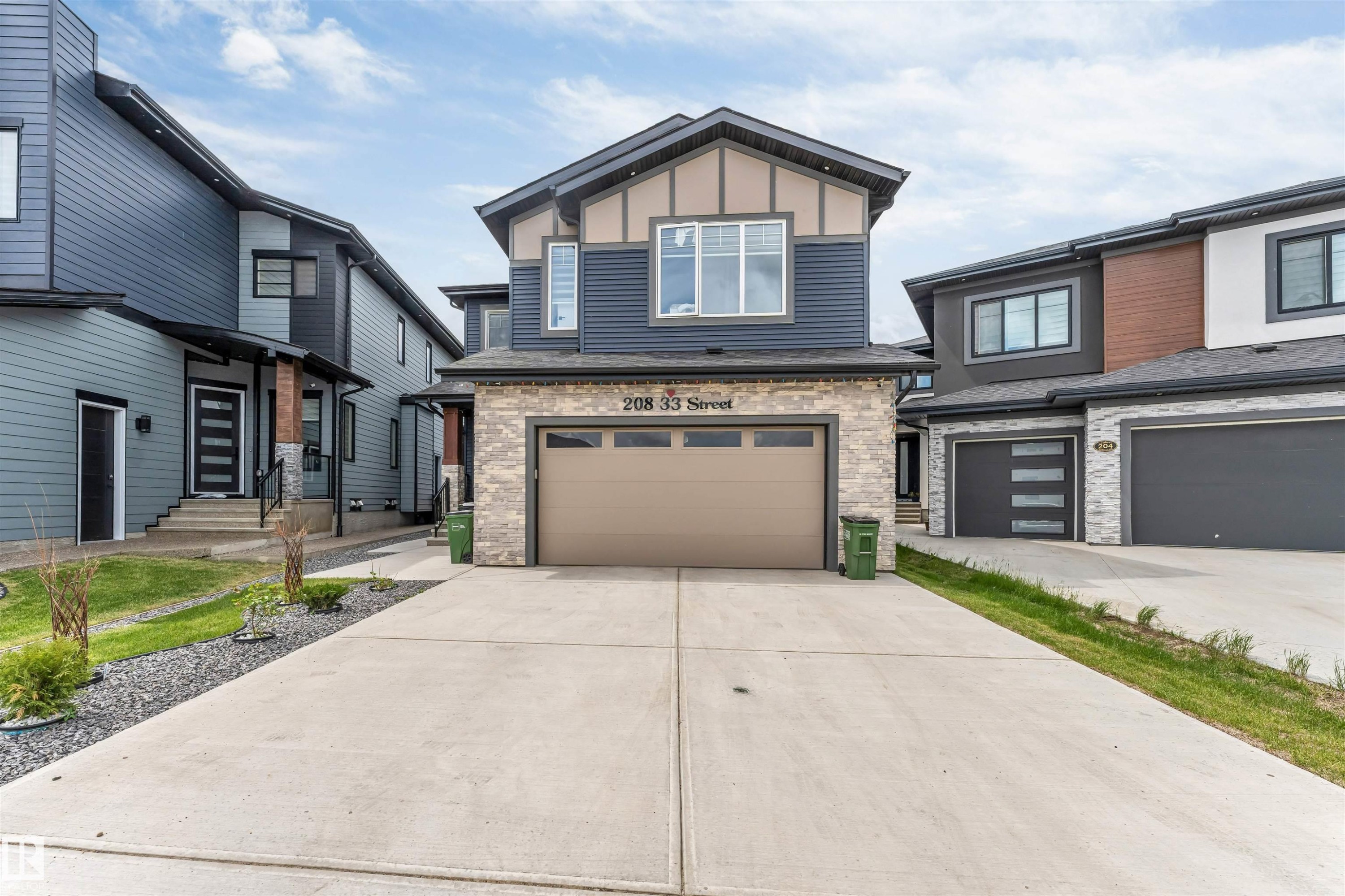 Modern two-story residence featuring a stone-clad garage, contemporary blue siding, contrasting beige accents, a paved driveway, and large windows - 208 33 Street, Edmonton, AB